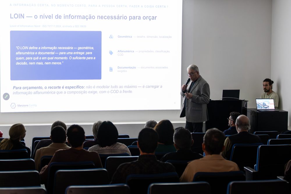 Plateia acompanhando a palestra, com o slide sobre nível de informação necessário projetado