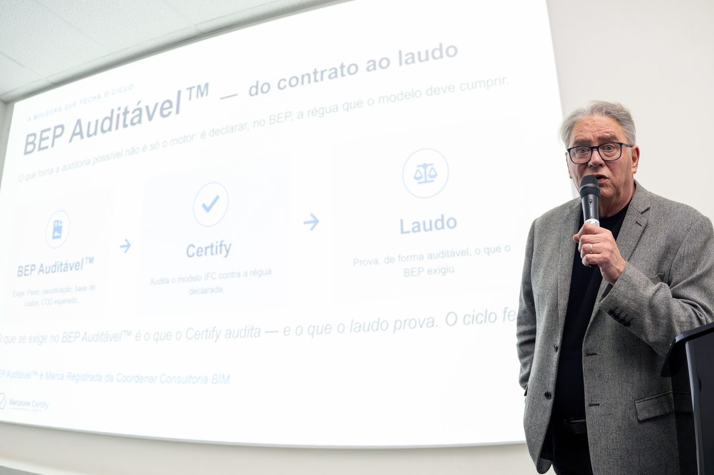 Leonardo Manzione em palestra, ao lado do slide que apresenta o ciclo do BEP Auditável, do contrato ao laudo